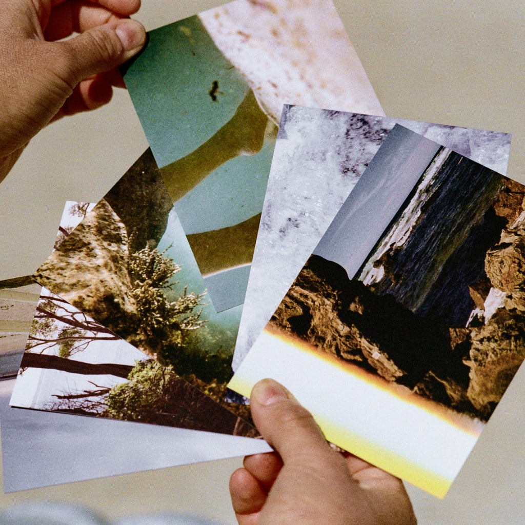 A fan of Coast Cards postcards held in two hands on the beach